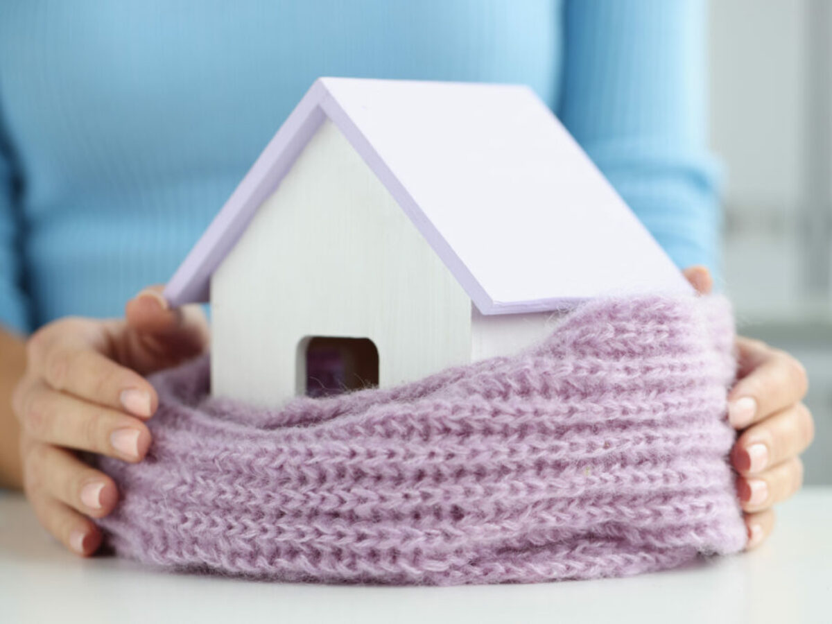 Woman wrapped small wooden house in warm scarf